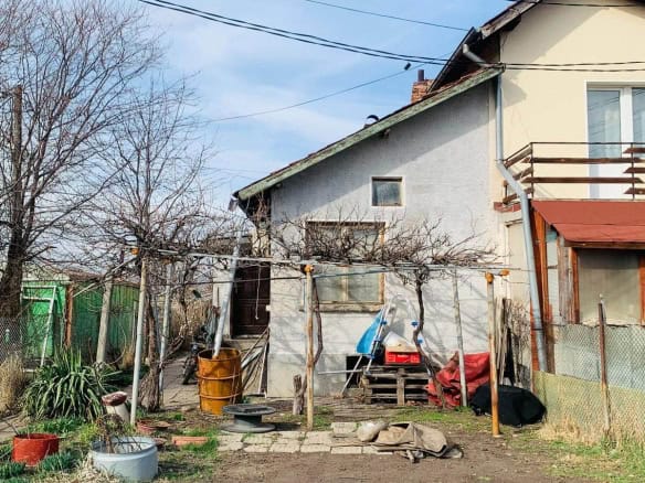 Къща с изглед към заден двор с ограда, множество дървета и външни съоръжения.