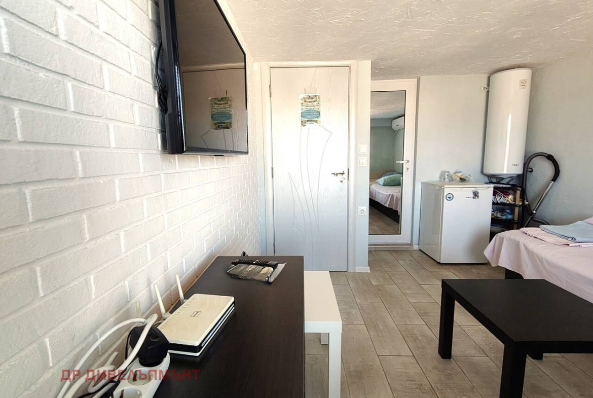 View of room with TV, dresser, door, mini fridge, and water heater