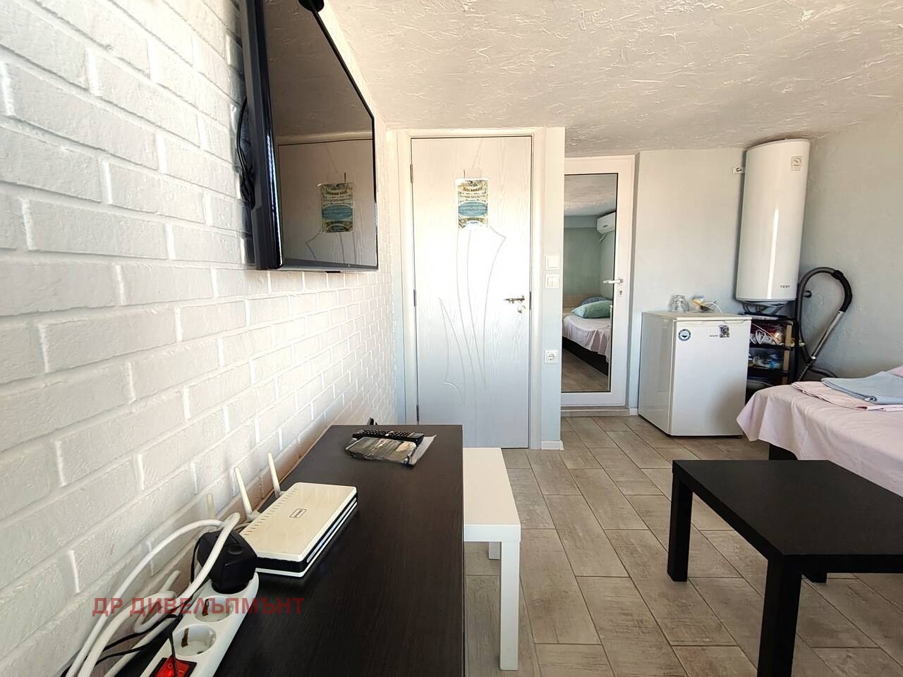 View of room with TV, dresser, door, mini fridge, and water heater