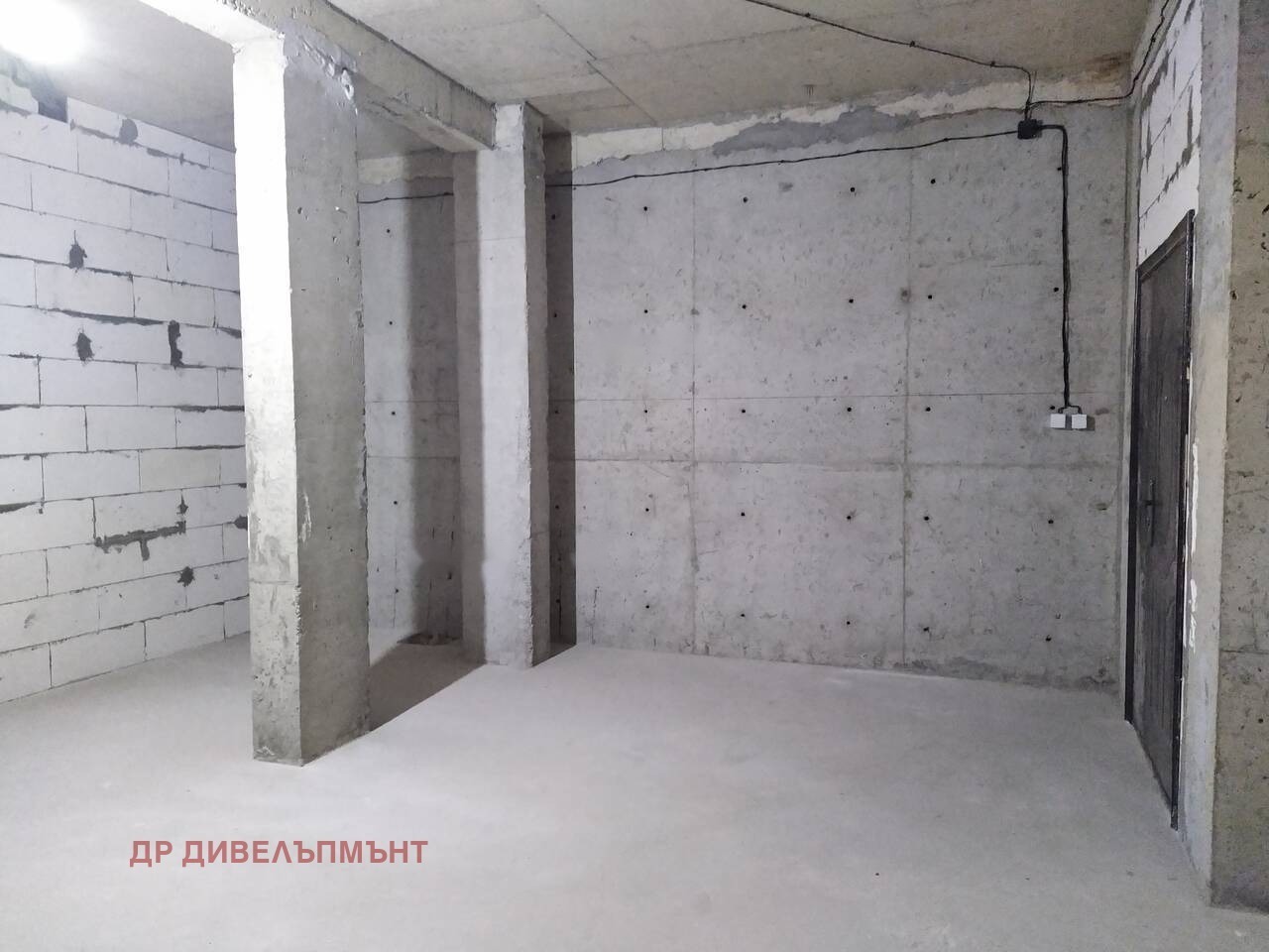 Необработено бетонно вътрешно пространство с блокови стени и отвор за врата