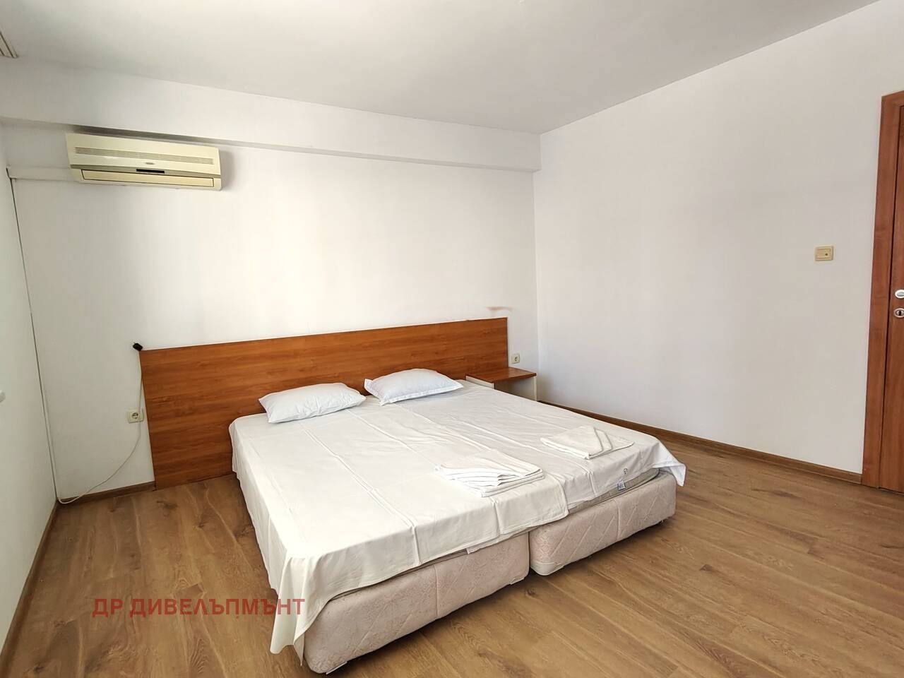 Bedroom with double bed, wooden headboard, wall-mounted air conditioner, and light wood floor