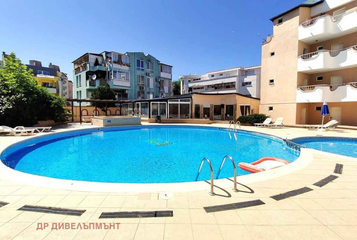 Large oval outdoor swimming pool with ladder, sun loungers, and adjacent building