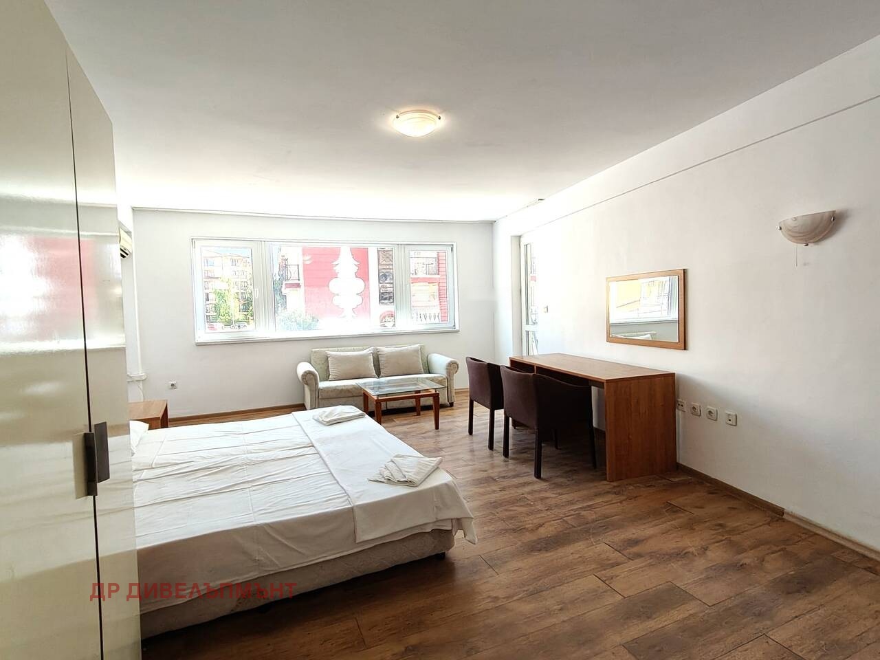 Bright room with double bed, desk with chairs, sofa, and large window