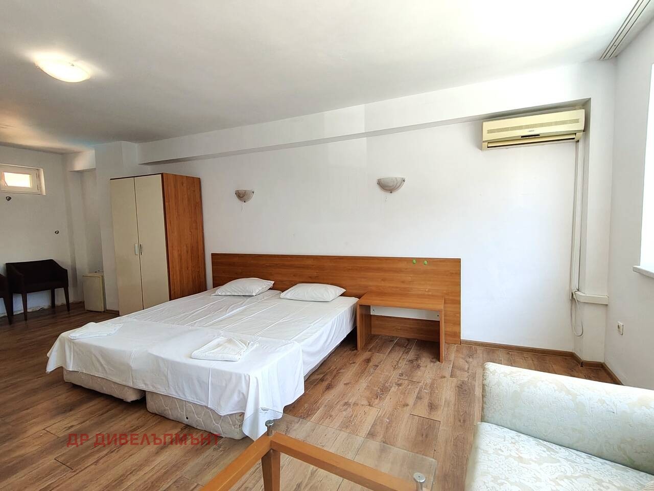 Bedroom with double bed, wooden headboard, wardrobe, wall-mounted air conditioner, and white walls