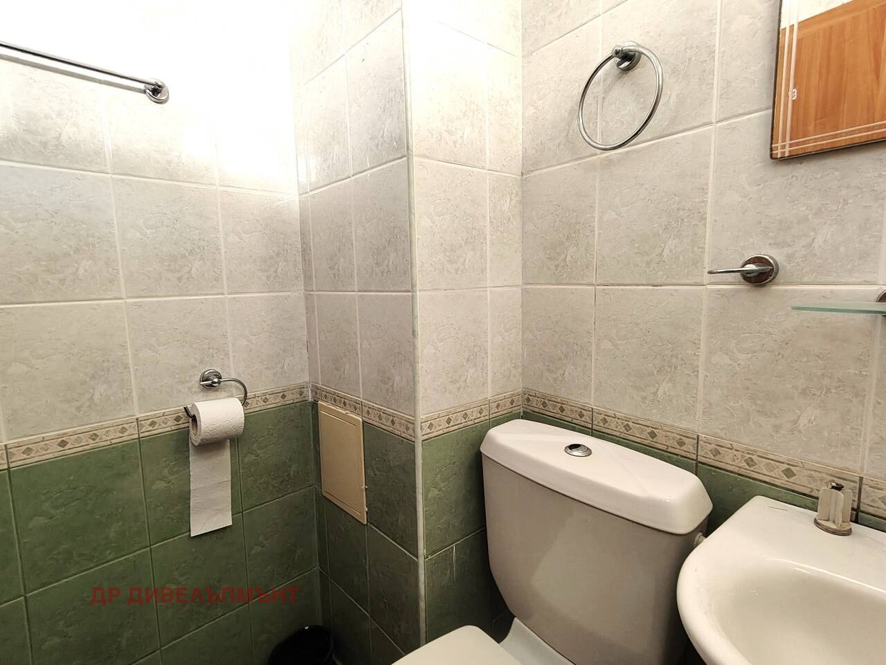 Bathroom corner showing toilet, pedestal sink, toilet roll holder, and tiled walls