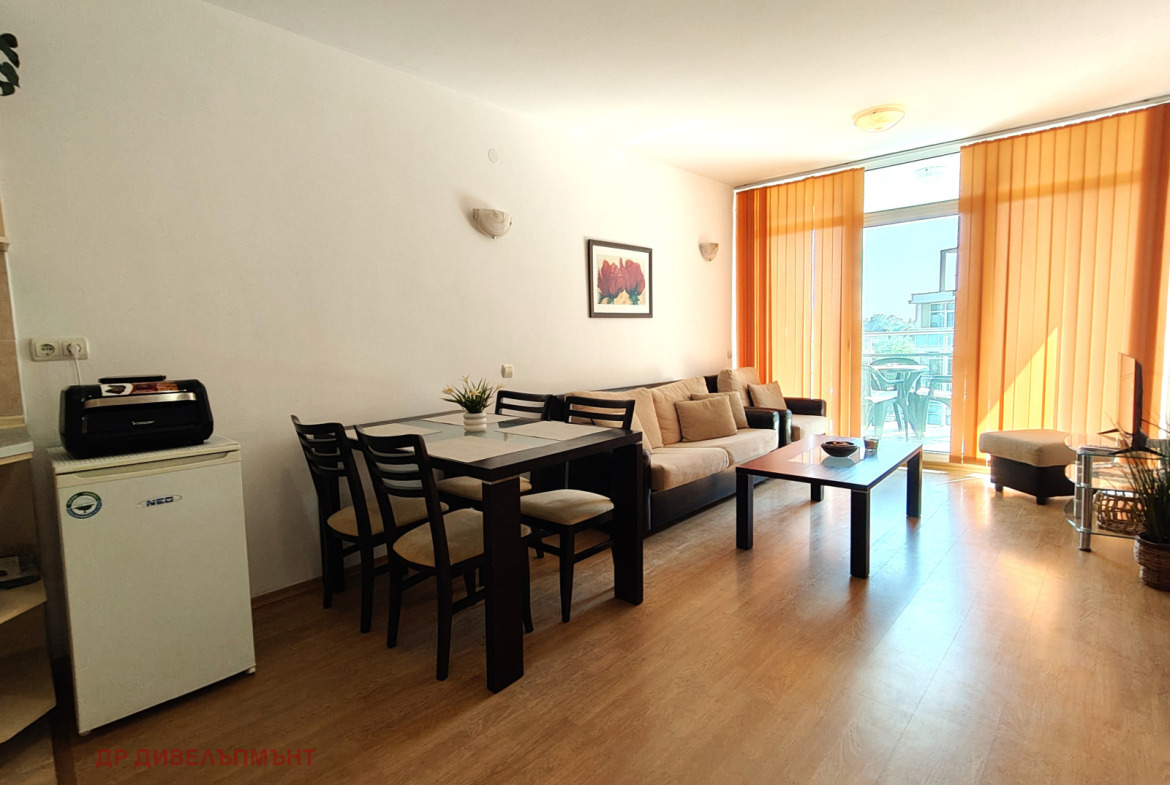 tristaen-apartament-95-kvm-pod-naem-kompleks-sani-holidey-nesebar-basein-parking-3 Светла всекидневна със софа и телевизор