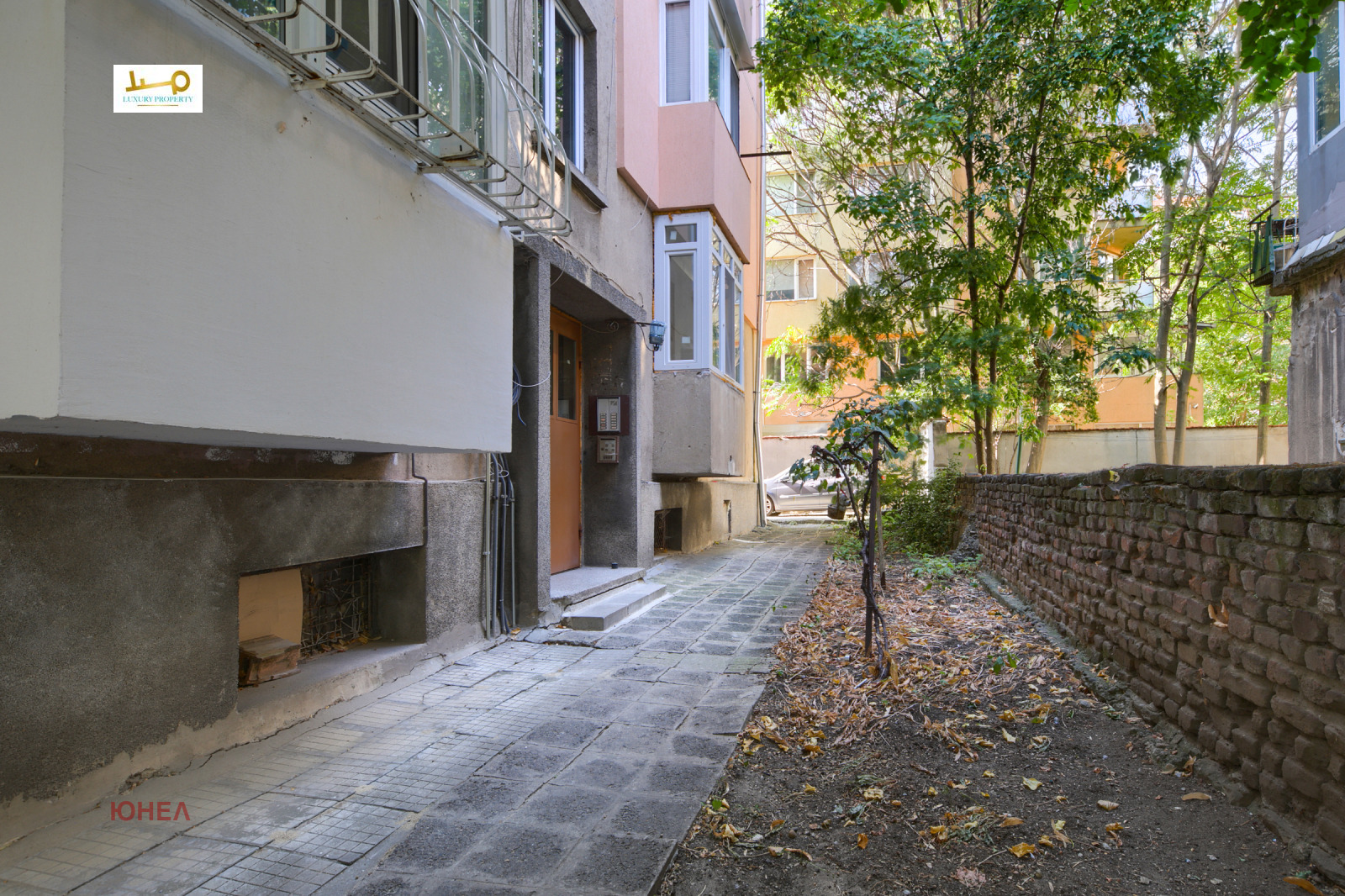 Narrow building entrance path with brick wall and trees