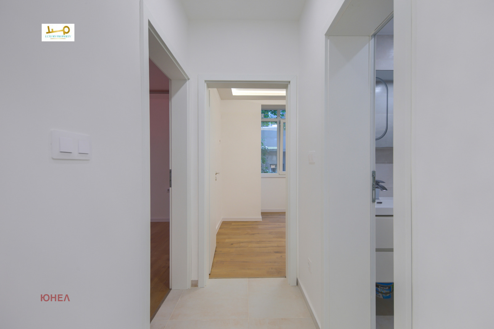 Hallway with three doorways leading to rooms and bathroom, tile floor, white walls