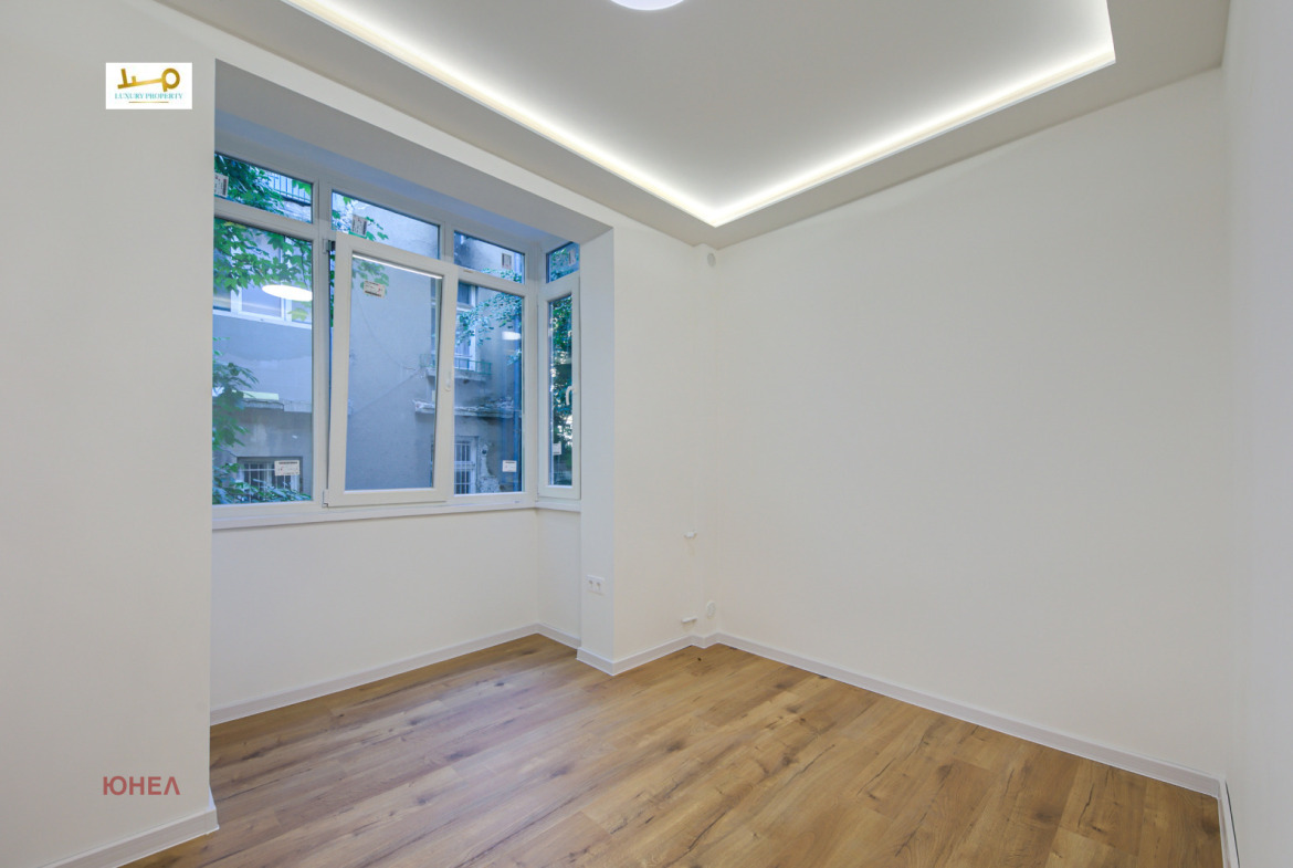 Room with large corner window, wood floor, LED cove ceiling lighting, white walls