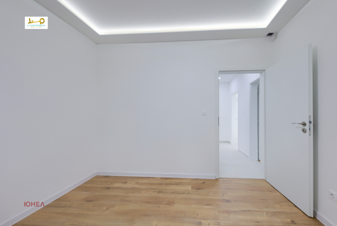 Empty room with wood floor, LED cove ceiling, white walls, open door to hallway