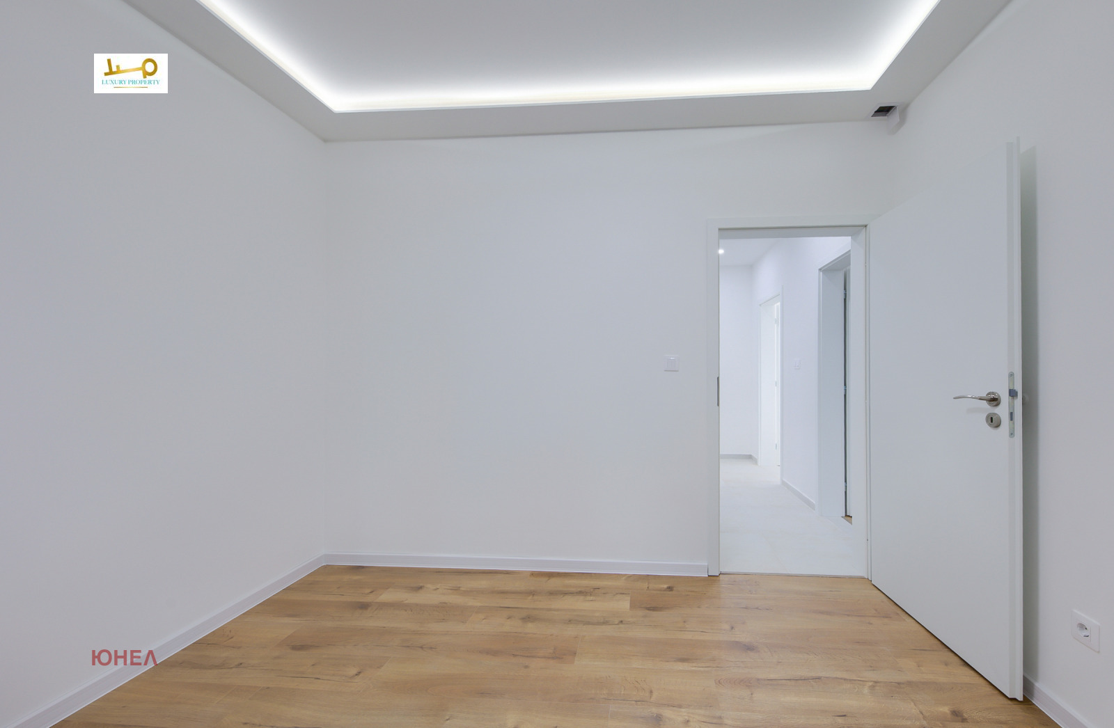 Empty room with wood floor, LED cove ceiling, white walls, open door to hallway