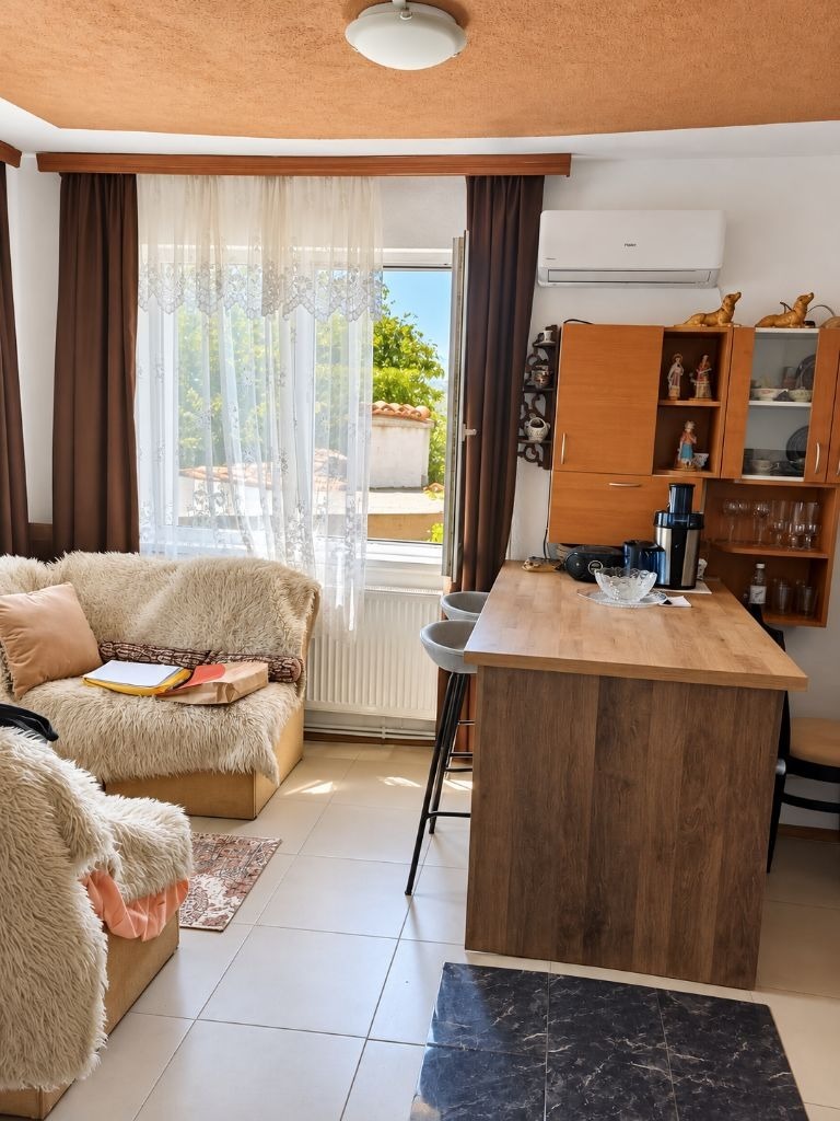 Living area with fur-covered armchair, wooden kitchen island, open balcony door, and wall-mounted air conditioner