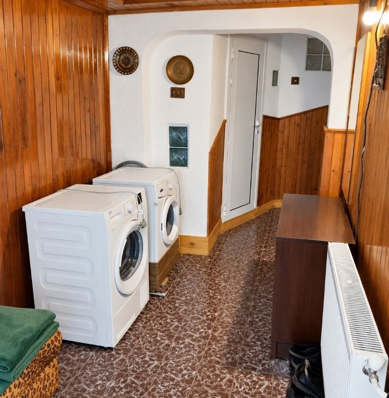 Utility room with two white washing machines, wood-paneled walls, and brown patterned floor