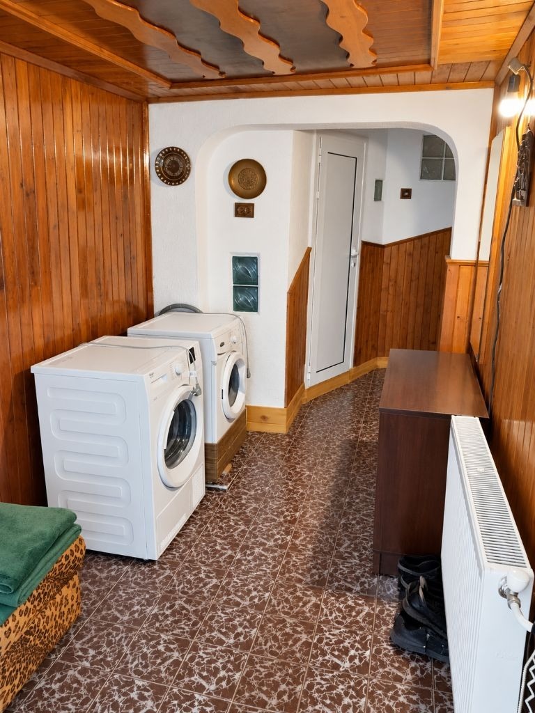 Utility room with two white washing machines, wood-paneled walls, and brown patterned floor