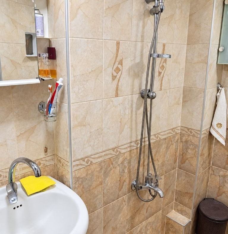 Bathroom with beige marble-style tiles, shower column, and wall-mounted sink