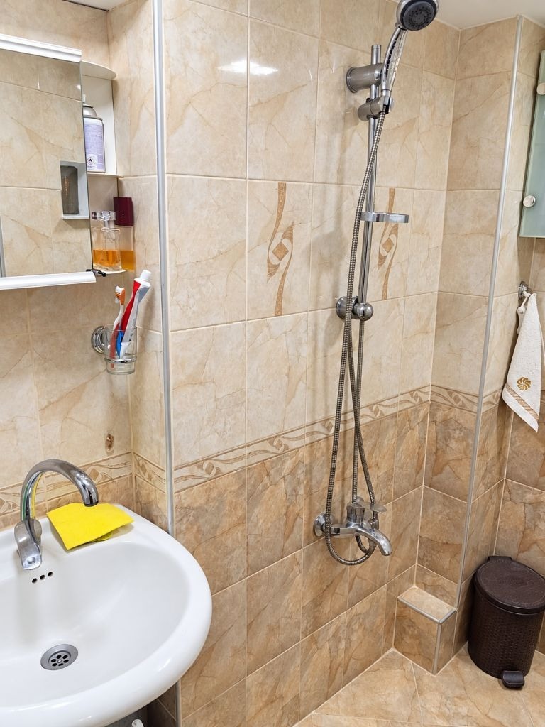 Bathroom with beige marble-style tiles, shower column, and wall-mounted sink