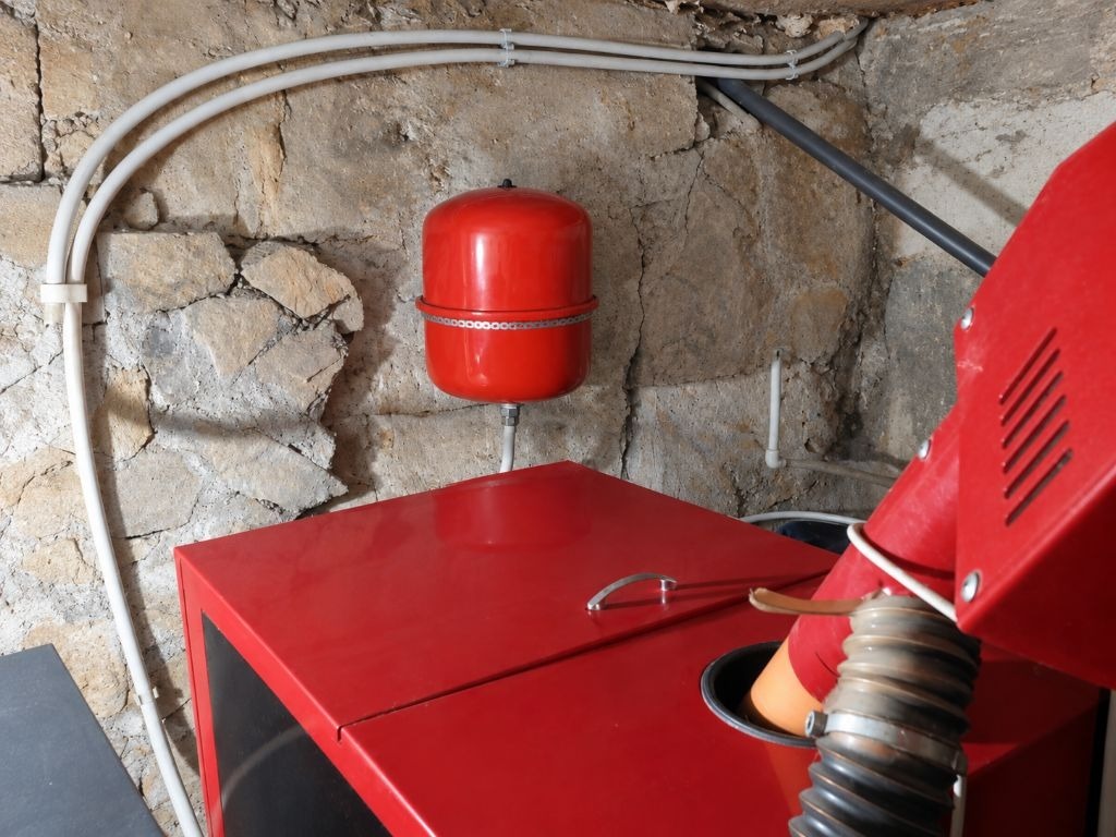 Red boiler and expansion tank mounted on stone wall with pipes