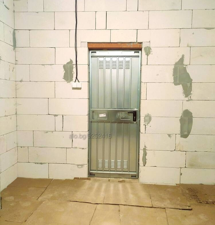 Metal security door with grate on brick wall