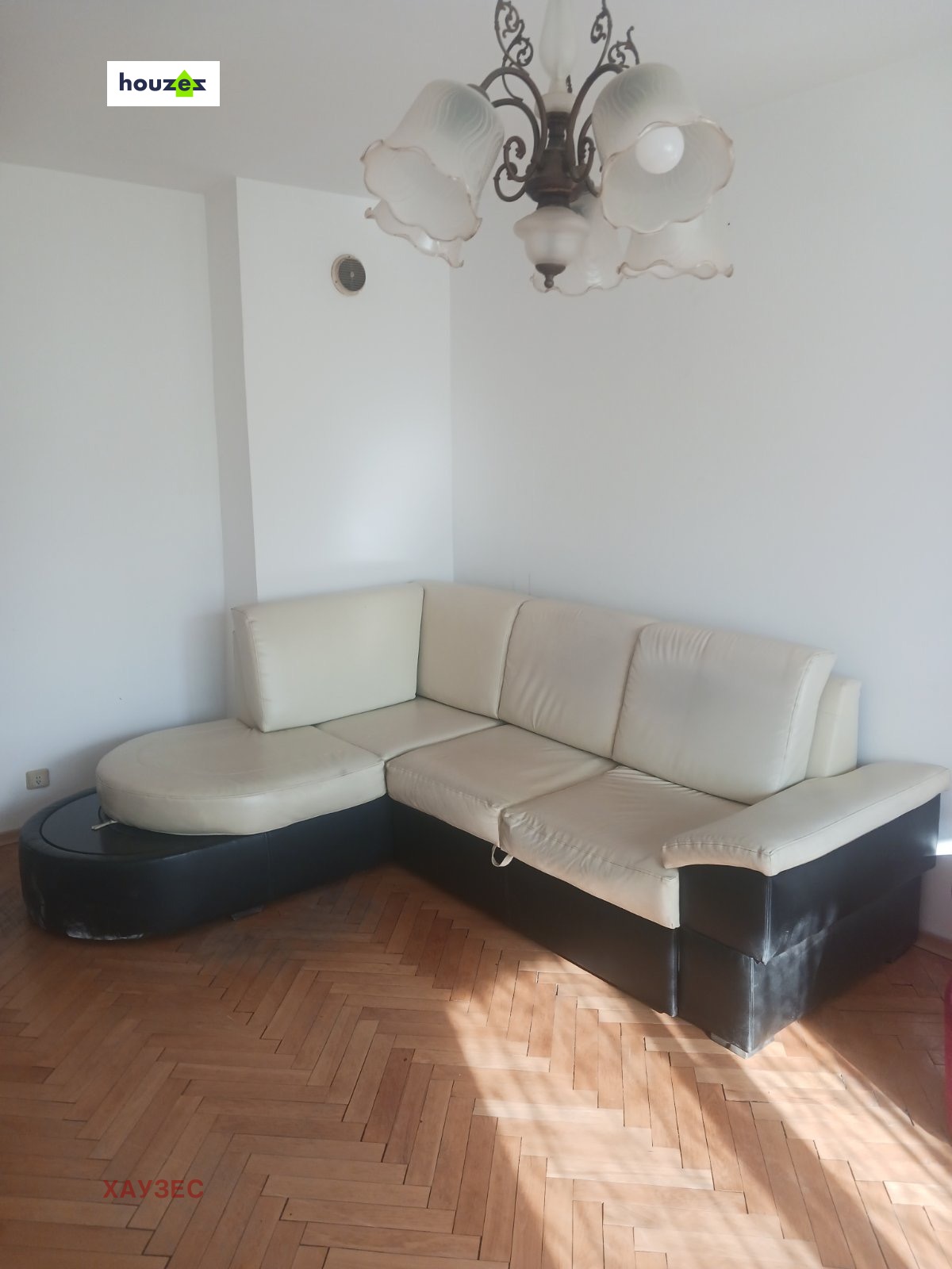 tristaen-apartament-90-sqm-pod-naem-lyulin-3-sofia-obzaveden-sklad-2 Хол с ъглов диван от кремава и тъмна кожа, паркетен под и полилей