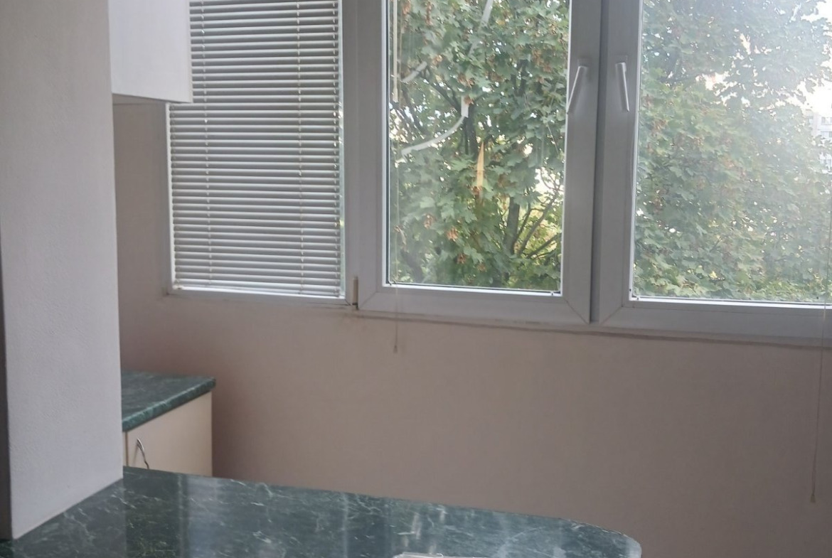 tristaen-apartament-90-sqm-pod-naem-lyulin-3-sofia-obzaveden-sklad-7 Кухненска трапезария със зелена мраморна маса, прозорец с щори и изглед към дървета