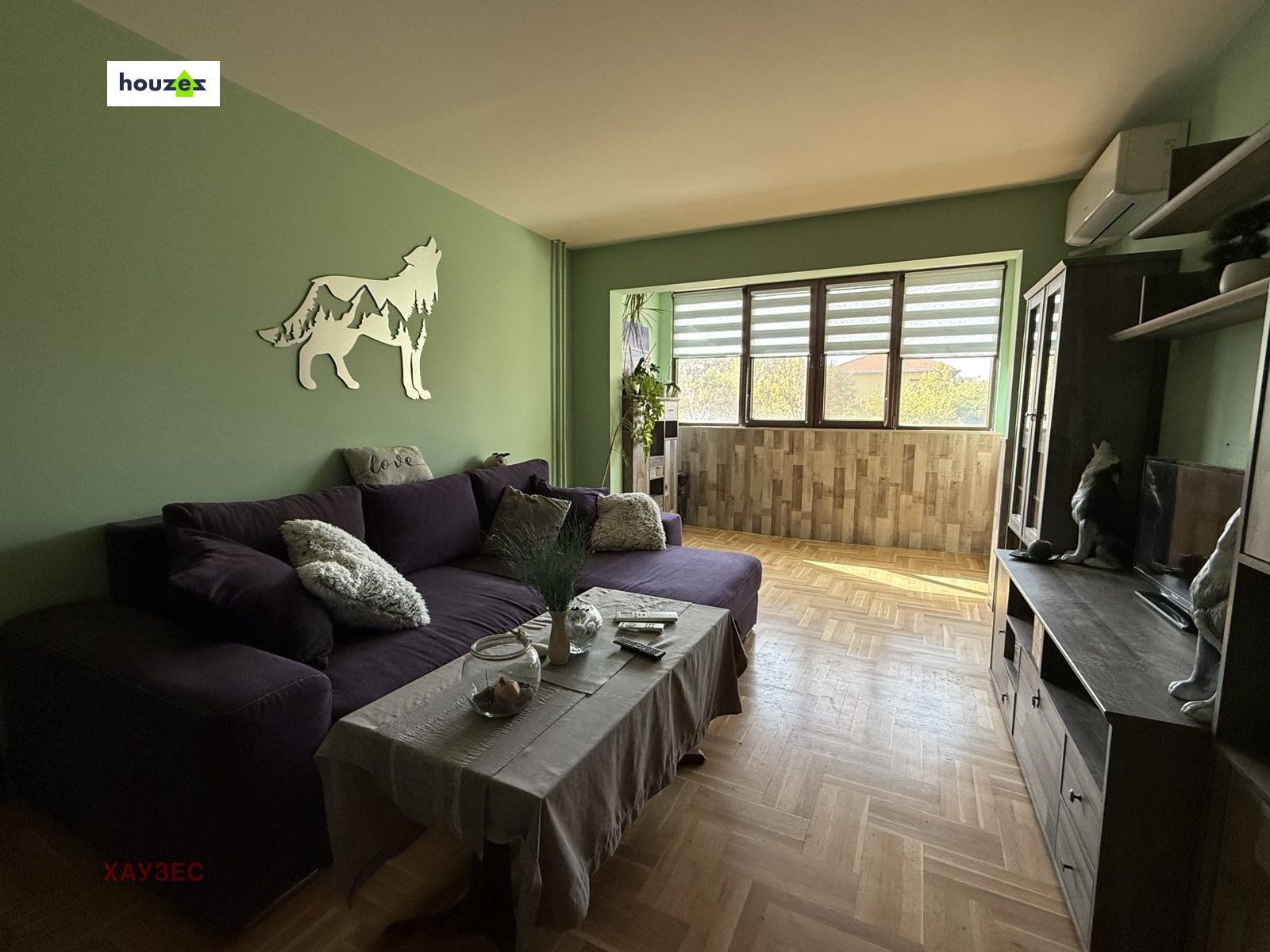 Living room with purple corner sofa, wolf wall decor, green walls, parquet floor