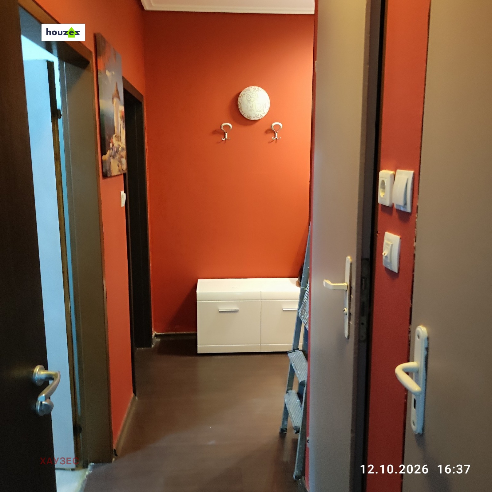 Narrow hallway with red walls, coat hooks, and white shoe cabinet