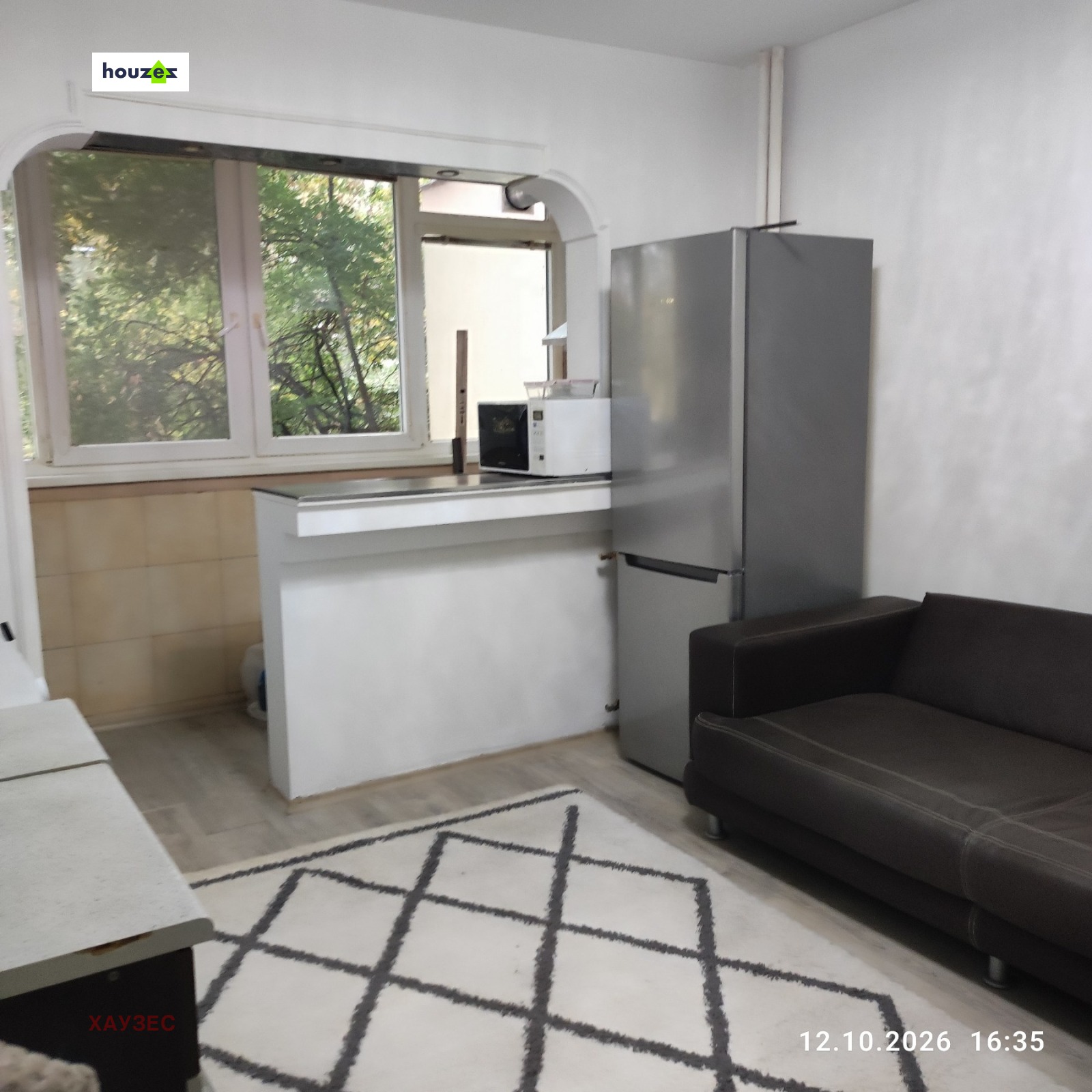 Kitchen area with stainless steel fridge, dark sofa, and large window