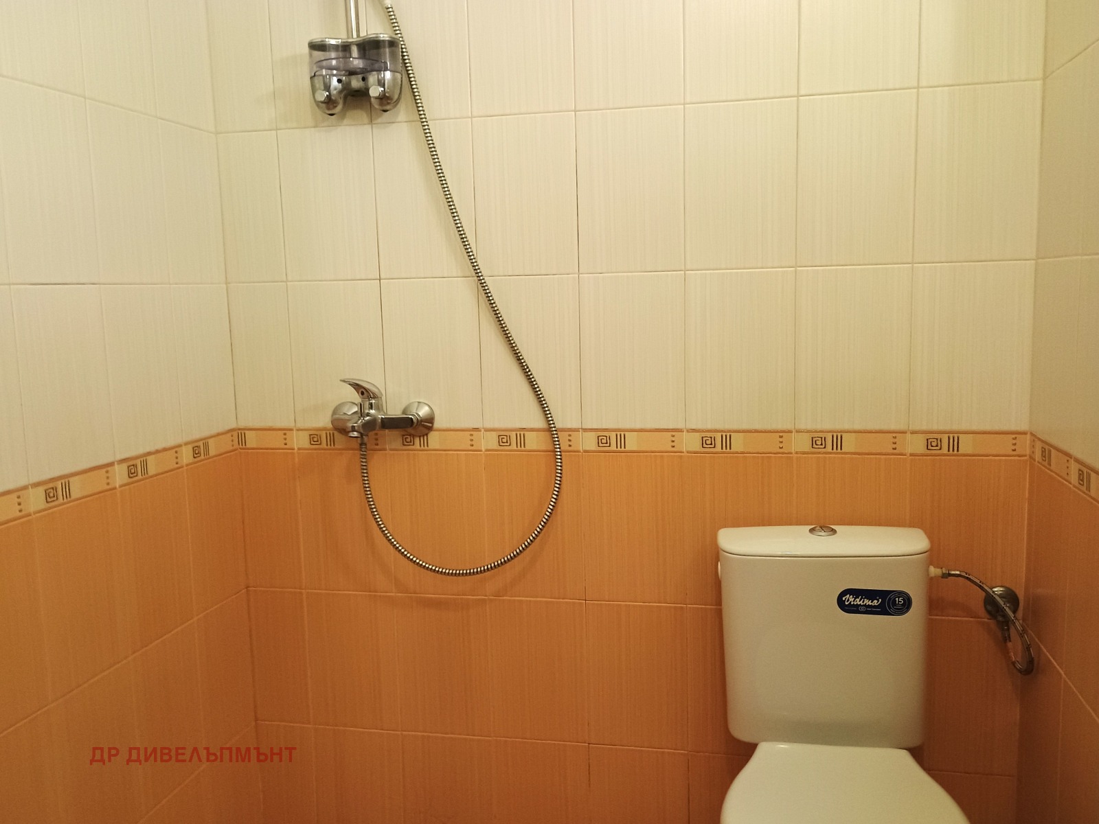 dvustaen-apartament-68-sqm-pod-naem-darvenitsa-sofiya-blizo-do-metro-10 Ъгъл на банята с тоалетна и стенен смесител с гъвкав маркуч, оранжеви плочки