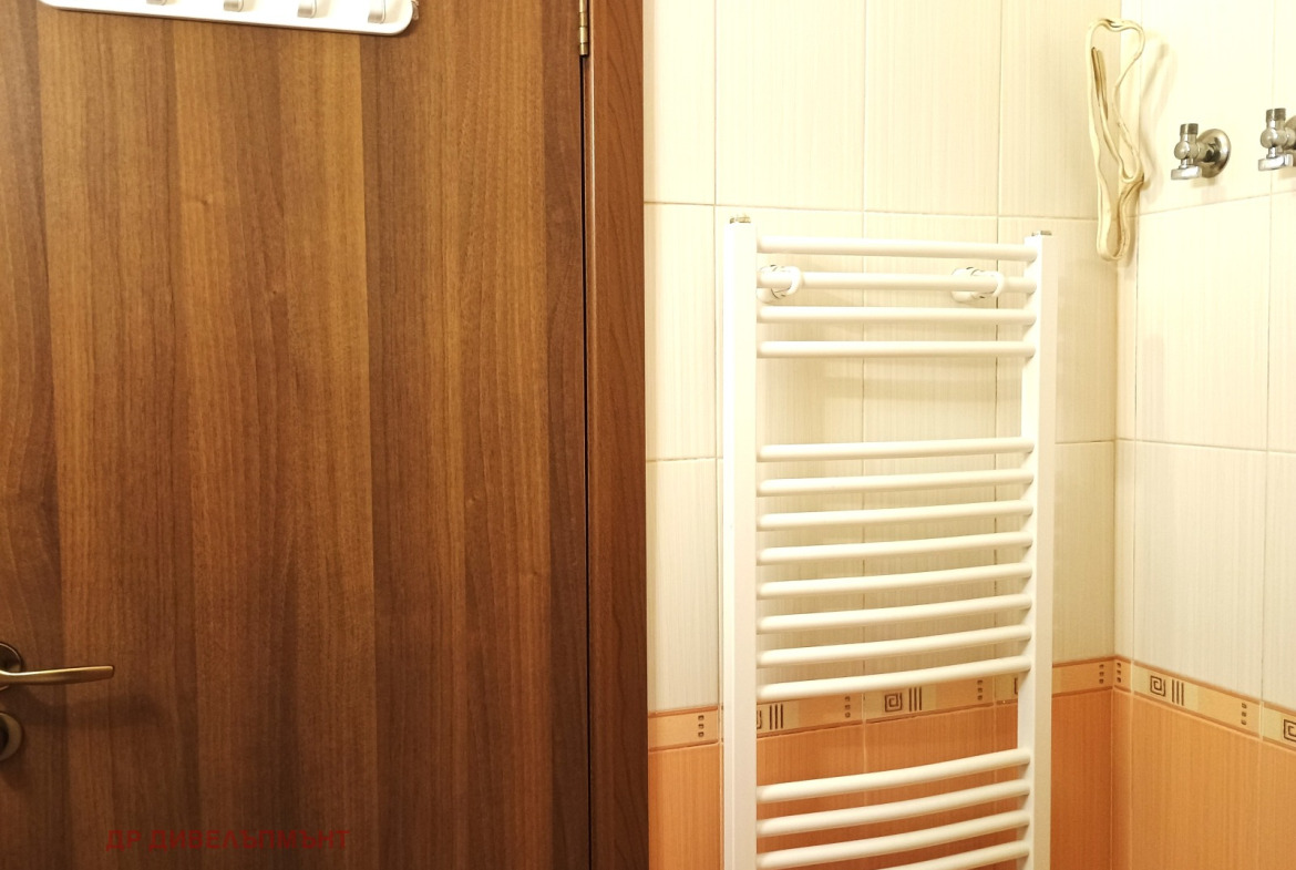 dvustaen-apartament-68-sqm-pod-naem-darvenitsa-sofiya-blizo-do-metro-11 Врата на банята с куки за дрехи и бял лира-радиатор на фона на облицована стена