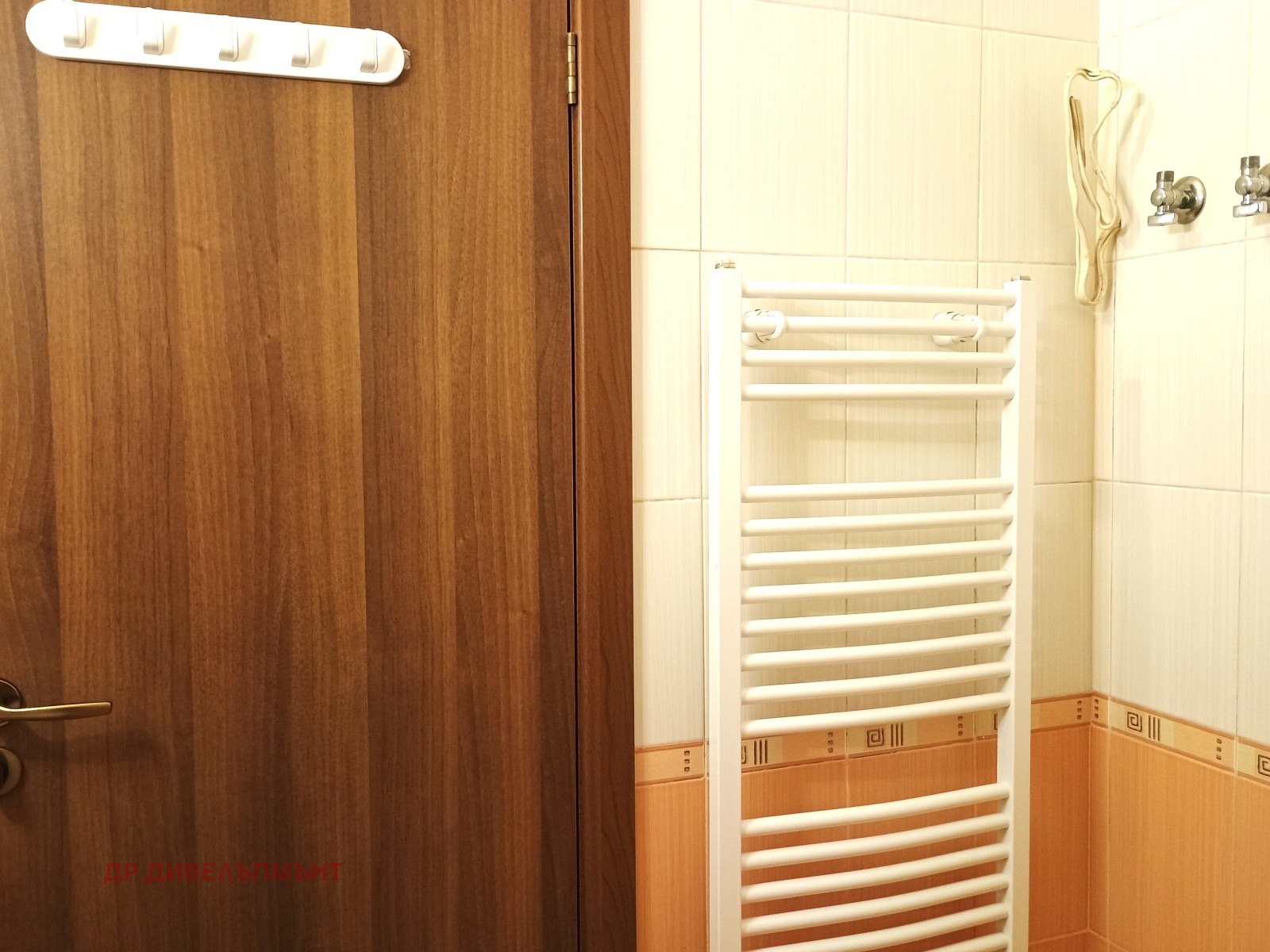 dvustaen-apartament-68-sqm-pod-naem-darvenitsa-sofiya-blizo-do-metro-11 Врата на банята с куки за дрехи и бял лира-радиатор на фона на облицована стена