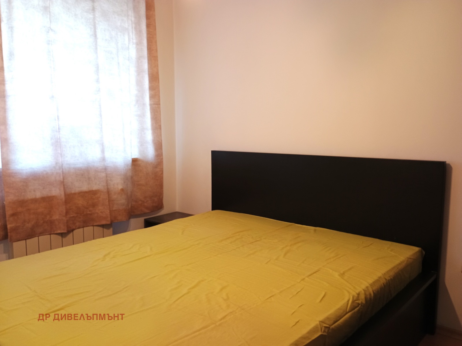 dvustaen-apartament-68-sqm-pod-naem-darvenitsa-sofiya-blizo-do-metro-12 Спалня с двойно легло, тъмно табло, жълта покривка и прозорец със завеси