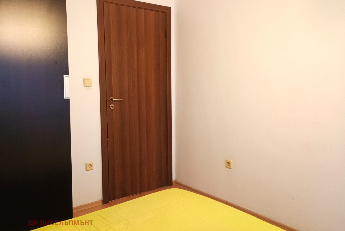 dvustaen-apartament-68-sqm-pod-naem-darvenitsa-sofiya-blizo-do-metro-14 Ъгъл на спалнята с ръб на тъмен гардероб, вътрешна врата и бели стени