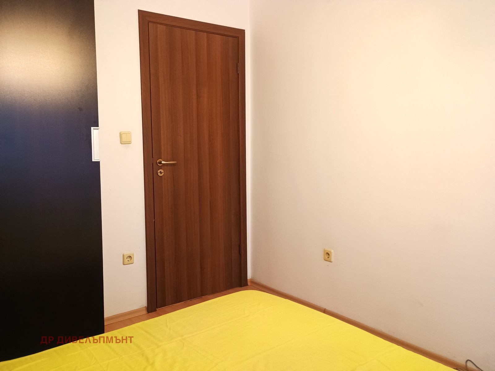 dvustaen-apartament-68-sqm-pod-naem-darvenitsa-sofiya-blizo-do-metro-14 Ъгъл на спалнята с ръб на тъмен гардероб, вътрешна врата и бели стени