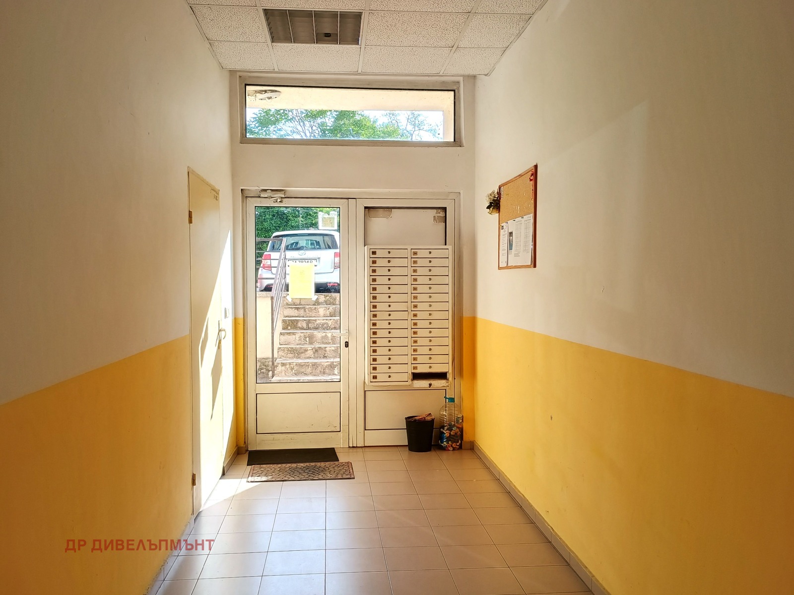 dvustaen-apartament-68-sqm-pod-naem-darvenitsa-sofiya-blizo-do-metro-17 Входно фоайе на сградата с пощенски кутии, стъклена входна врата и жълто боядисани долни стени