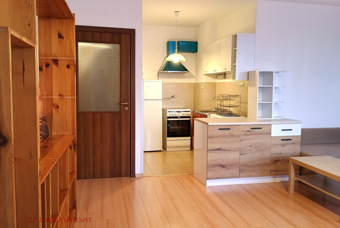 dvustaen-apartament-68-sqm-pod-naem-darvenitsa-sofiya-blizo-do-metro-2 Дневна с дървен рафт, врата и кухня на заден план