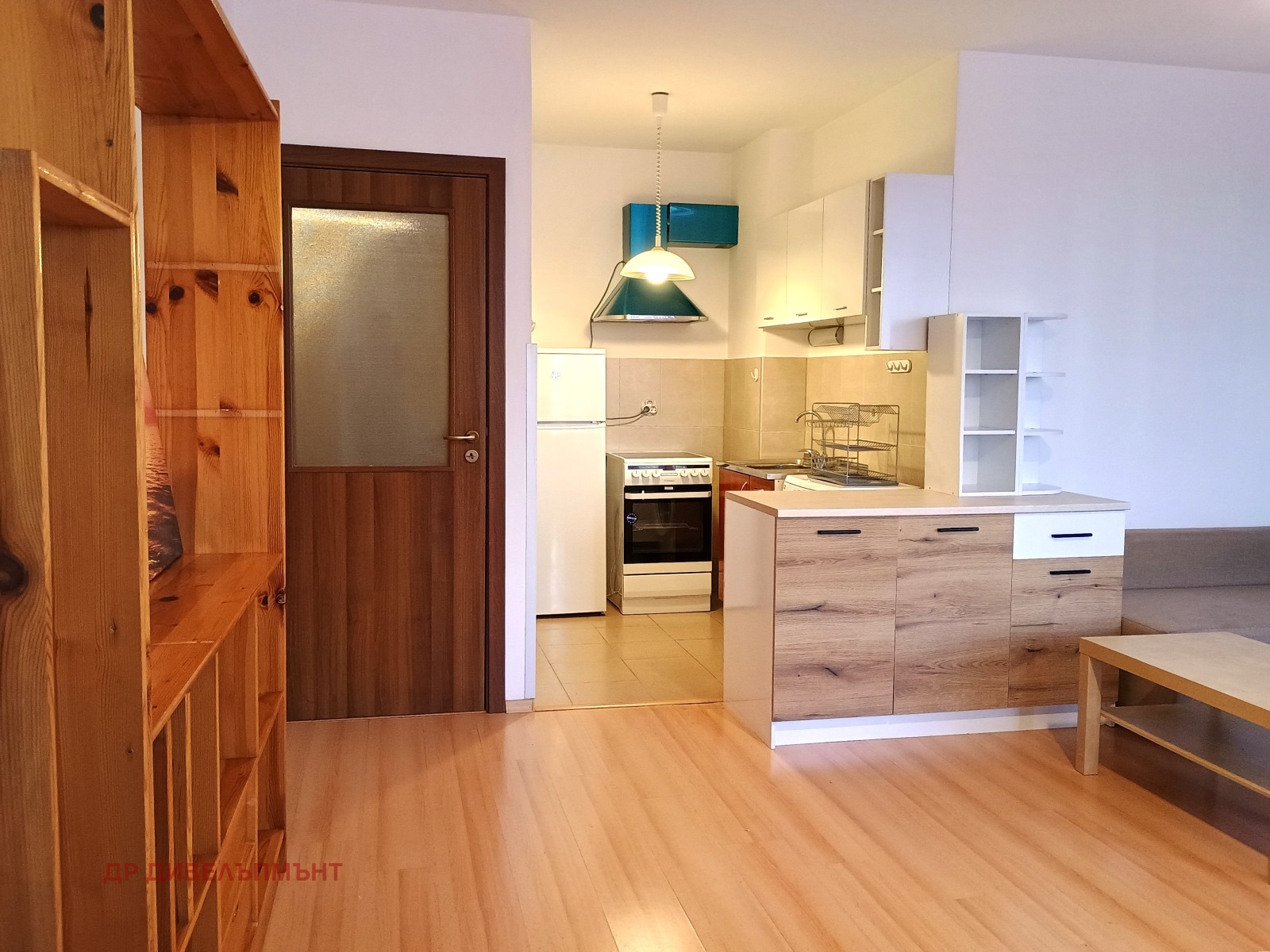 dvustaen-apartament-68-sqm-pod-naem-darvenitsa-sofiya-blizo-do-metro-2 Дневна с дървен рафт, врата и кухня на заден план