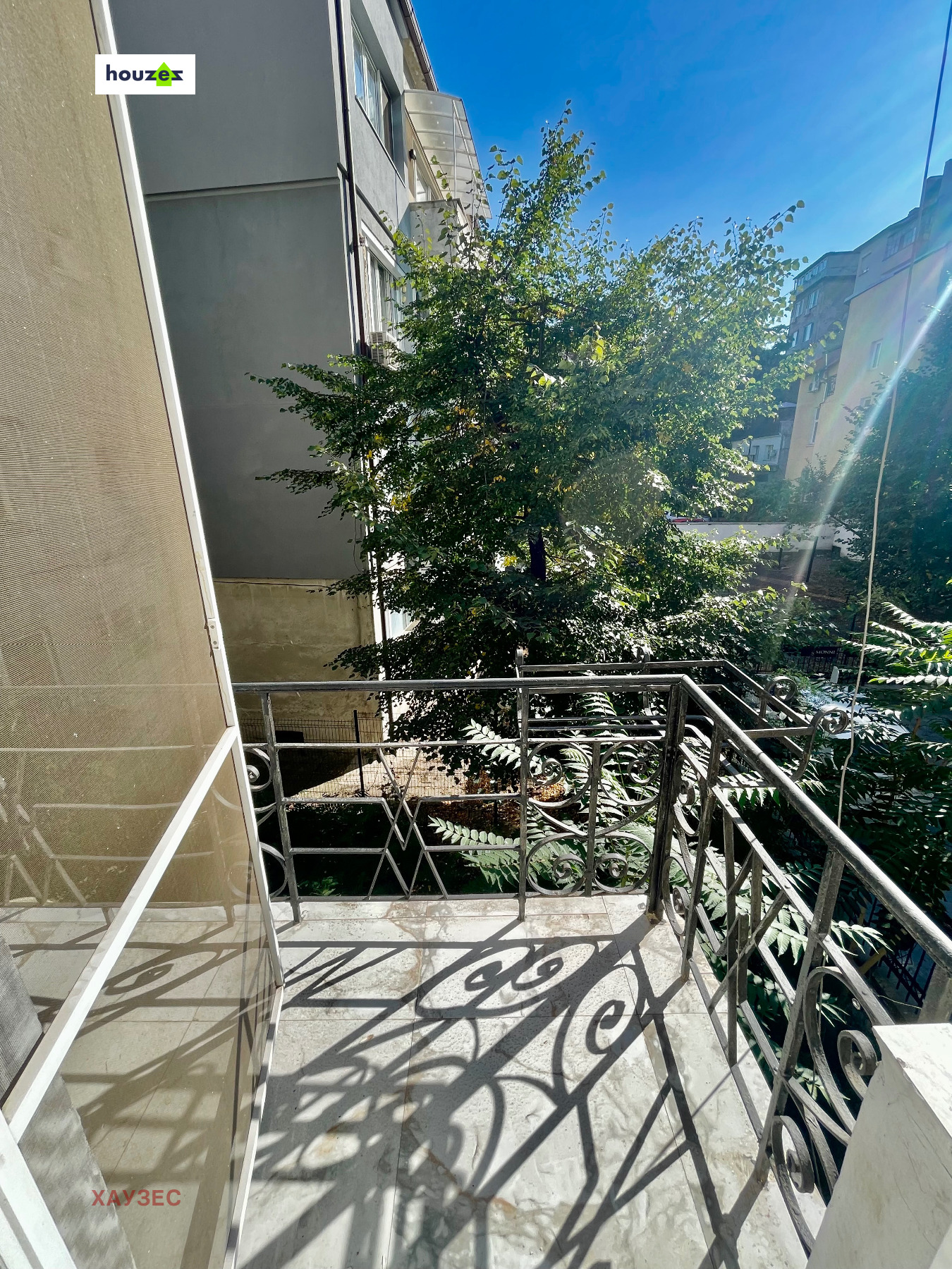Balcony with wrought iron railing overlooking trees and neighbouring buildings