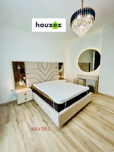Bedroom with upholstered bed, mirrored headboard panels, round vanity mirror, chandelier