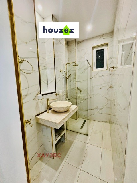 Marble-tiled bathroom with glass shower, stone vessel sink, gold fixtures