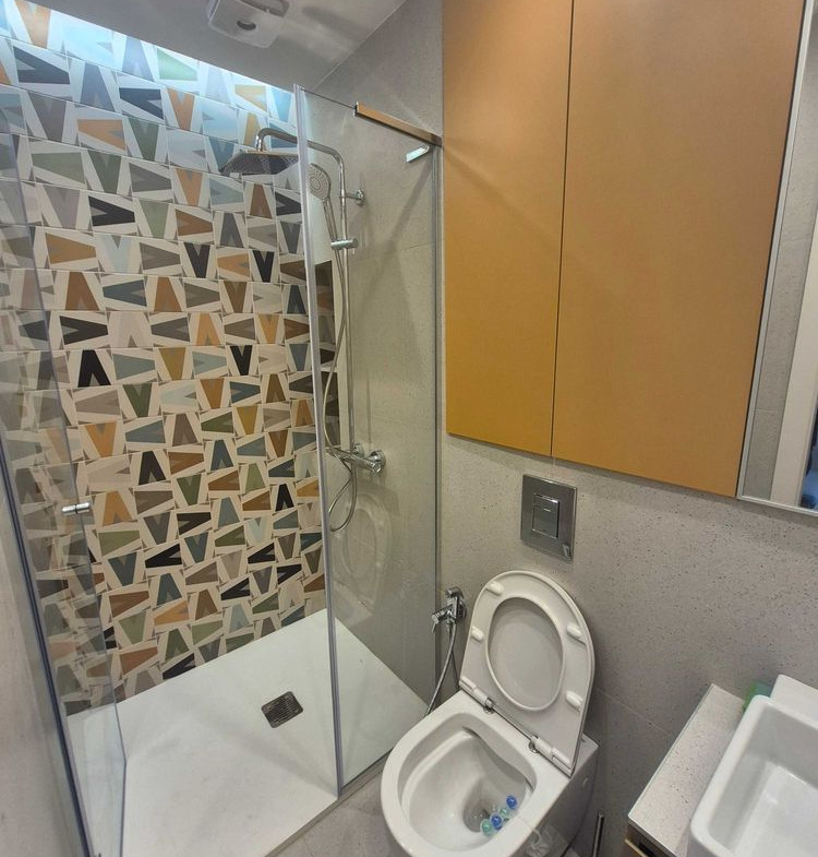 dvustaen-apartament-73-sqm-pod-naem-manastirski-livadi-sgrada-diada-10 Баня със стъклена душ кабина, цветни геометрични плочки, окачена тоалетна, оранжев шкаф