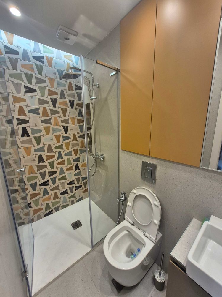 dvustaen-apartament-73-sqm-pod-naem-manastirski-livadi-sgrada-diada-10 Баня със стъклена душ кабина, цветни геометрични плочки, окачена тоалетна, оранжев шкаф
