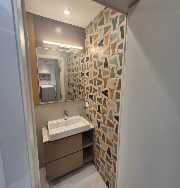 dvustaen-apartament-73-sqm-pod-naem-manastirski-livadi-sgrada-diada-12 Изглед към банята през вратата с мивка тип купа, голямо огледало, стена с цветни триъгълни плочки