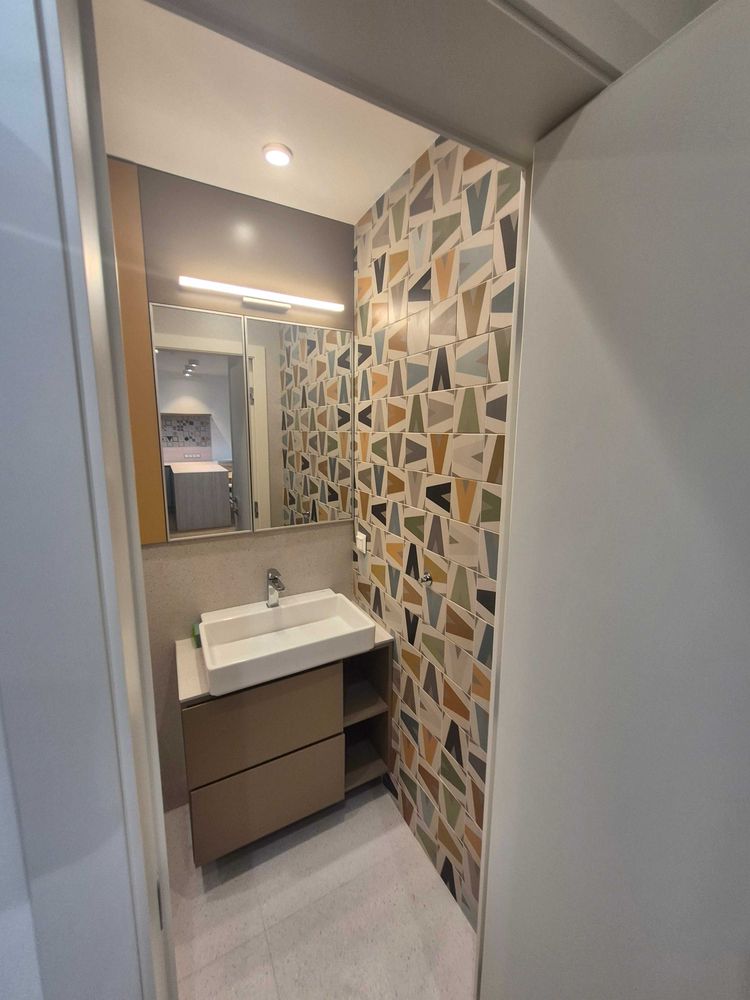 dvustaen-apartament-73-sqm-pod-naem-manastirski-livadi-sgrada-diada-12 Изглед към банята през вратата с мивка тип купа, голямо огледало, стена с цветни триъгълни плочки