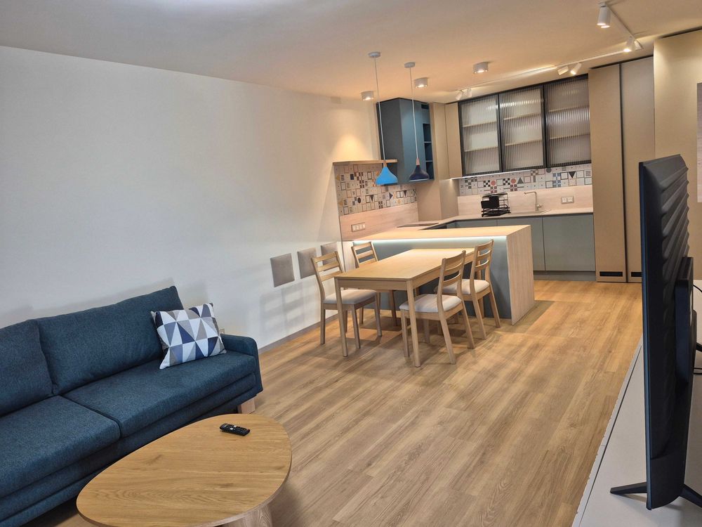 dvustaen-apartament-73-sqm-pod-naem-manastirski-livadi-sgrada-diada-4 Отворено пространство с хол и трапезария, синьо диван, дървена маса, кухня се вижда на заден план
