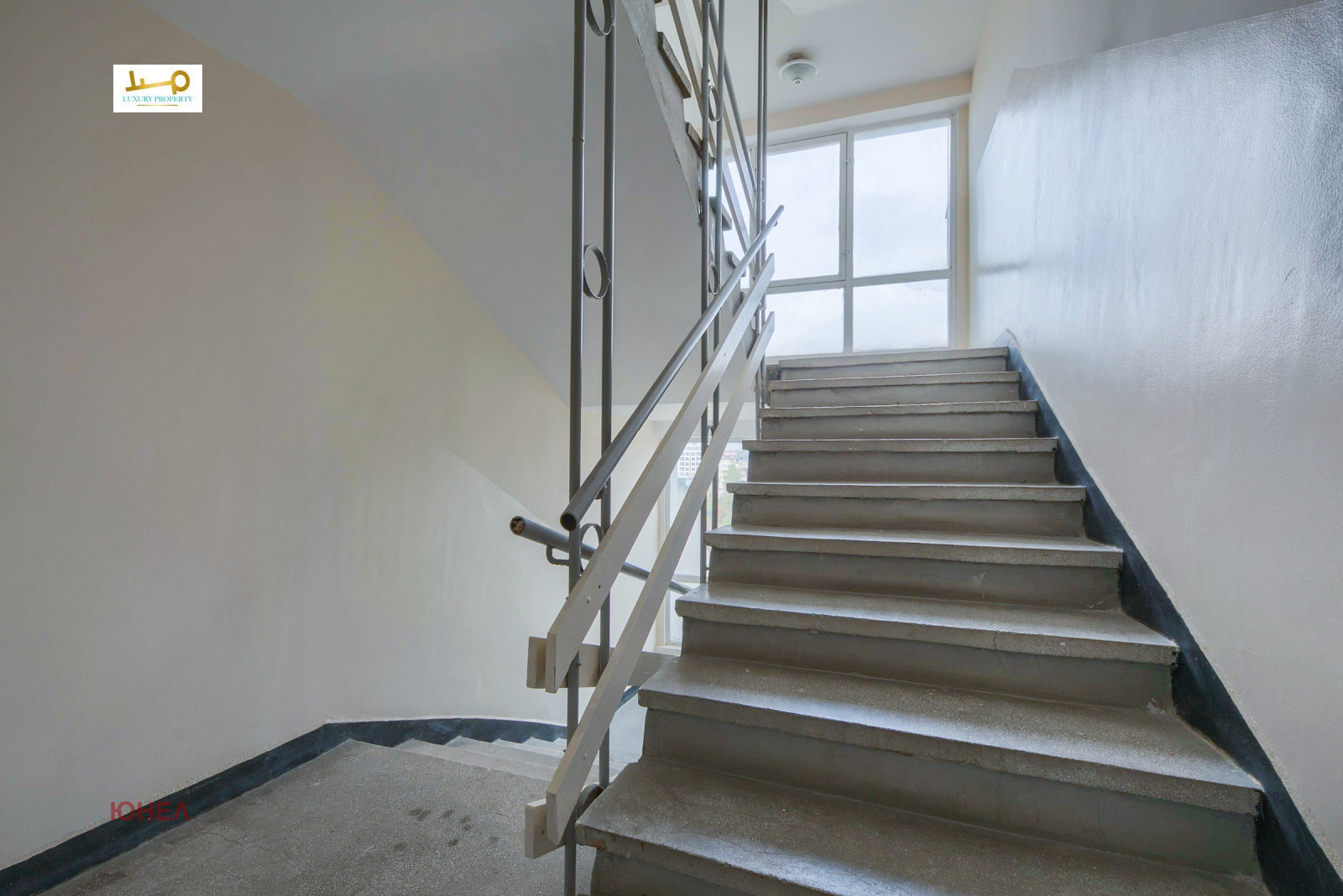 Common staircase with concrete steps, metal railing and large window on landing