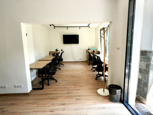 Office in Sofia with two long wooden desks, black chairs, wall-mounted TV, and balcony door