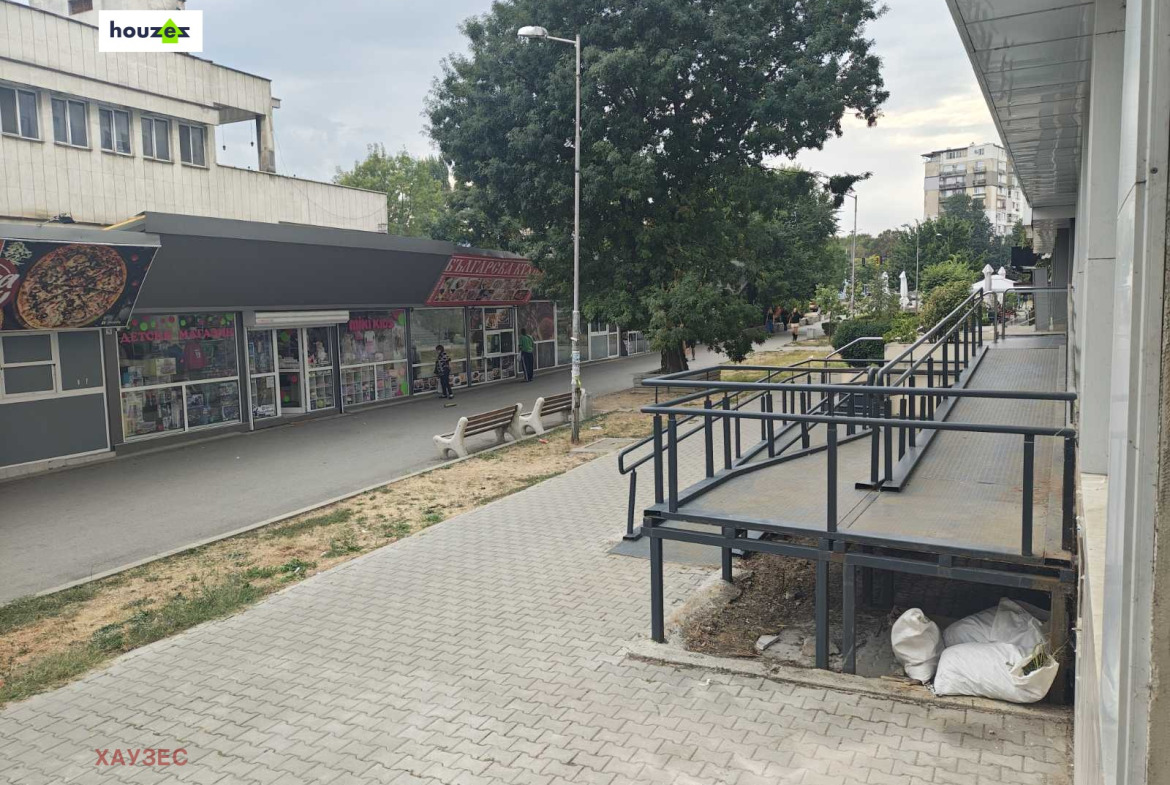 Външна пешеходна зона с парапети на рампа, магазини и дървета наоколо