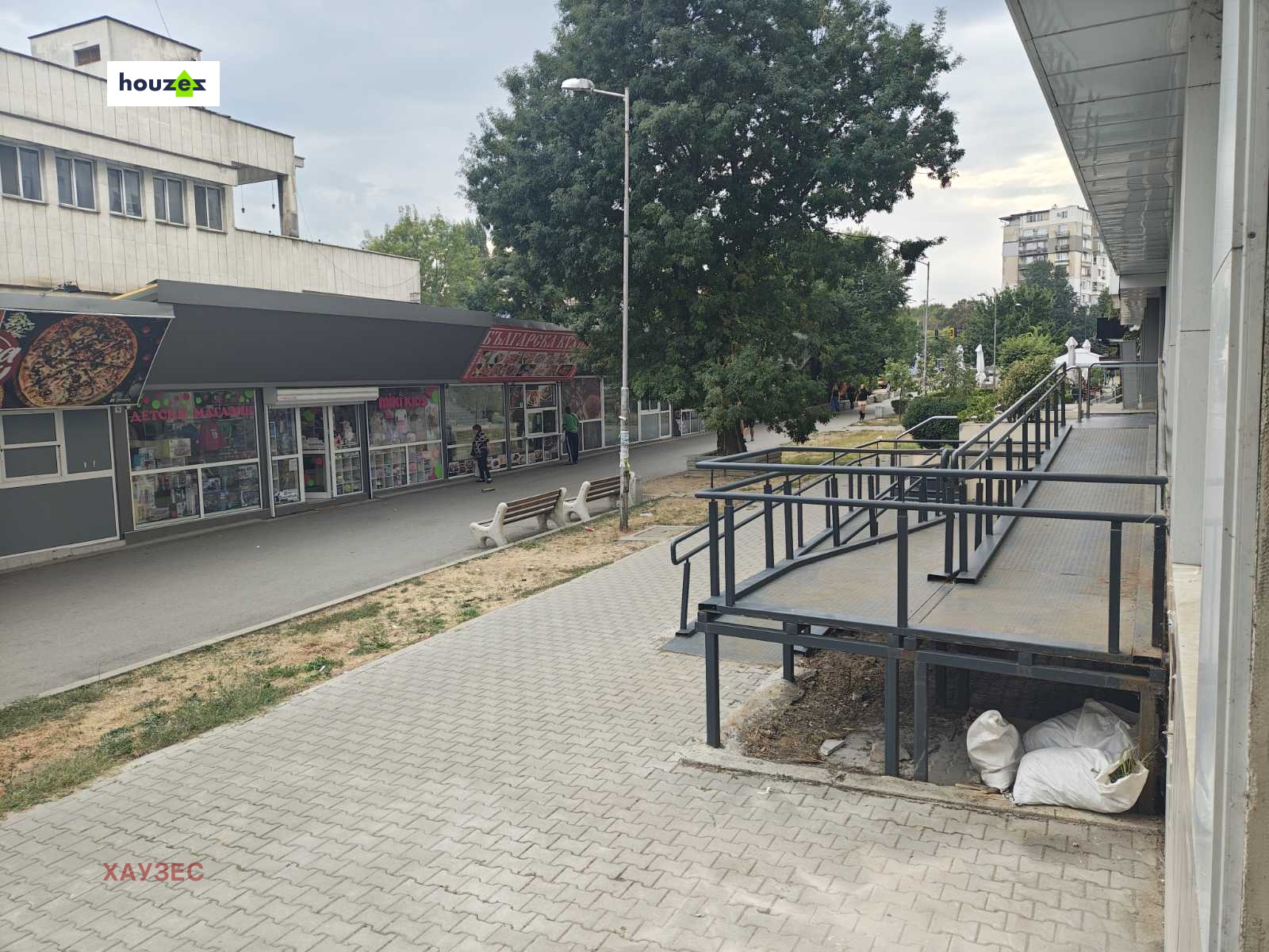 Външна пешеходна зона с парапети на рампа, магазини и дървета наоколо