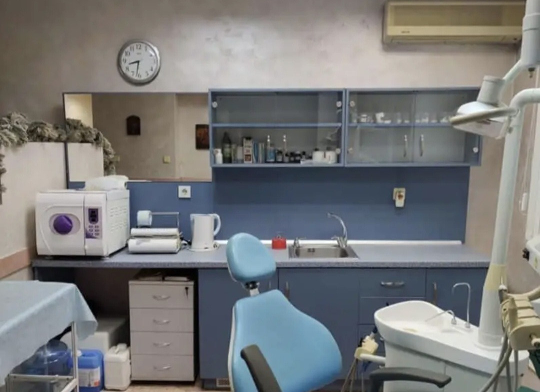 Dental office with blue cabinetry, autoclave, sink, and patient chair