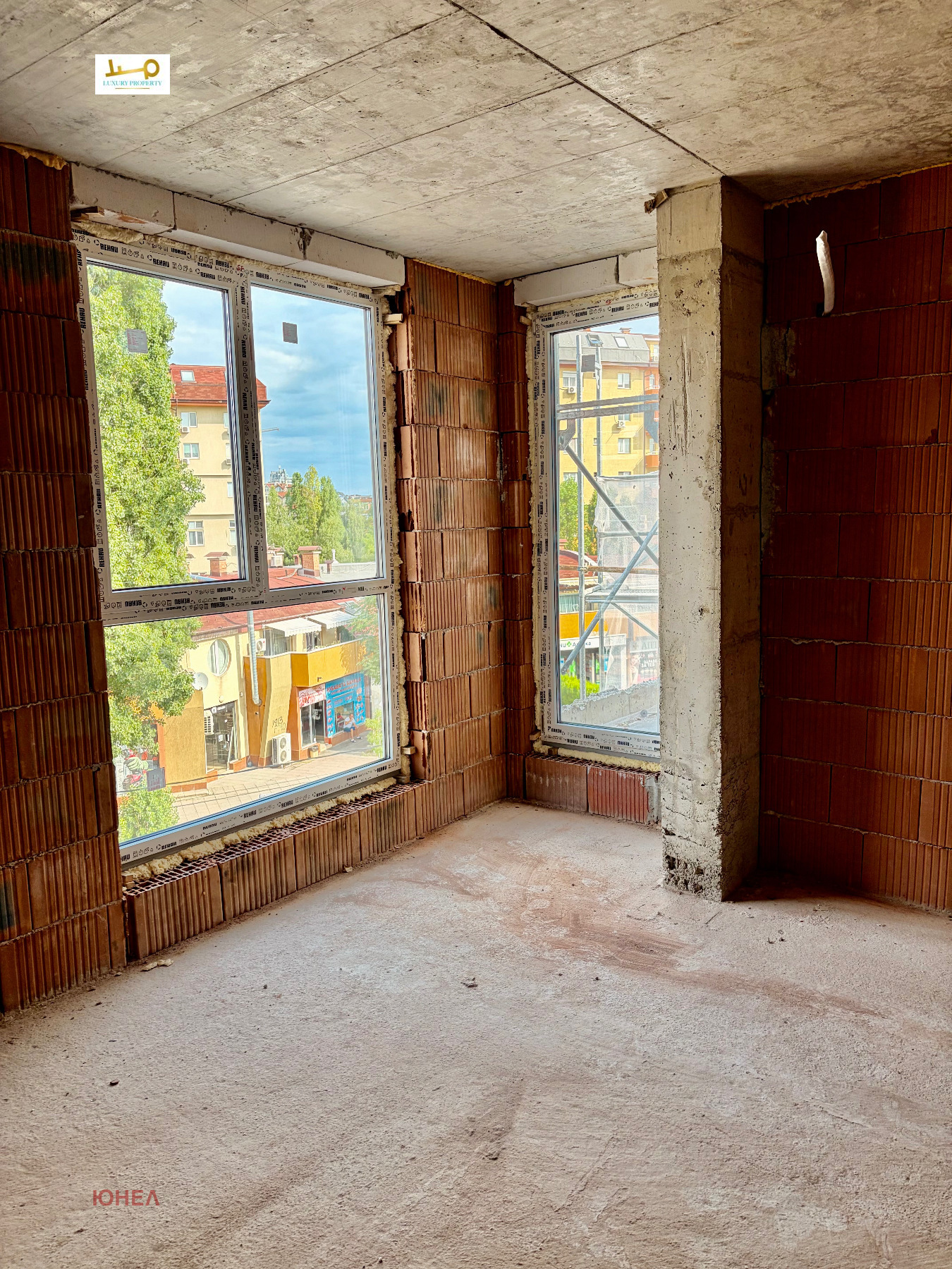 tristaen-apartament-108-sqm-za-prodazhba-ovcha-kupel-novo-stroitelstvo-8 Недовършена стая с два ъглови прозореца с изглед към улица, дървета и съседни сгради